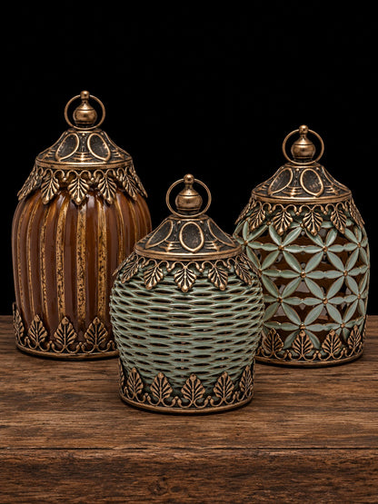 Tres faroles decorativos con acabado dorado envejecido, uno rayado caramelo y dos verdes, sobre mesa de madera rústica
