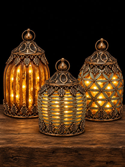 Tres faroles decorativos encendidos con luz cálida y acabado dorado envejecido, sobre mesa de madera rústica