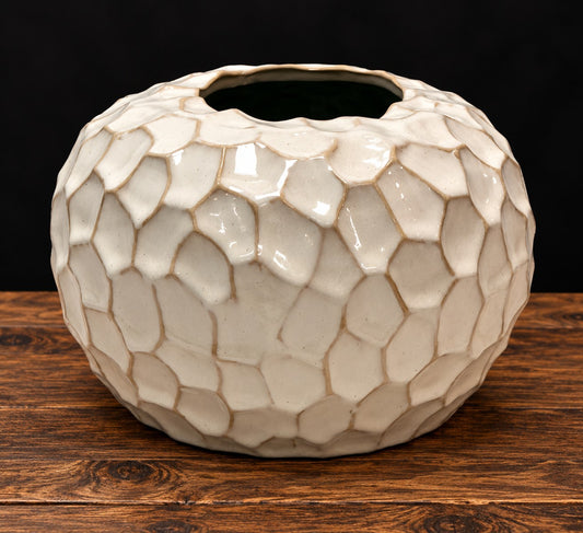 Jarrón redondo de cerámica esmaltada blanco roto con relieve de escamas sobre mesa de madera