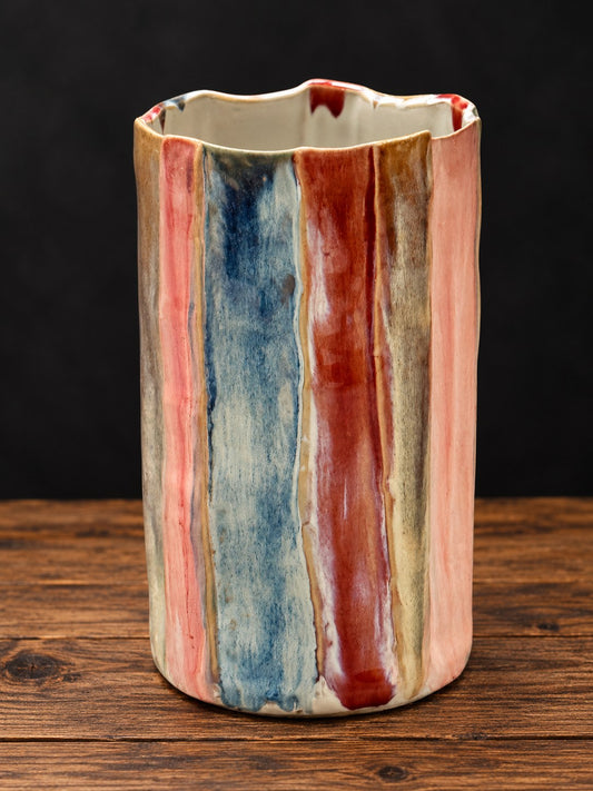 Jarrón de cerámica esmaltada con rayas rosas, azules y rojas sobre mesa de madera