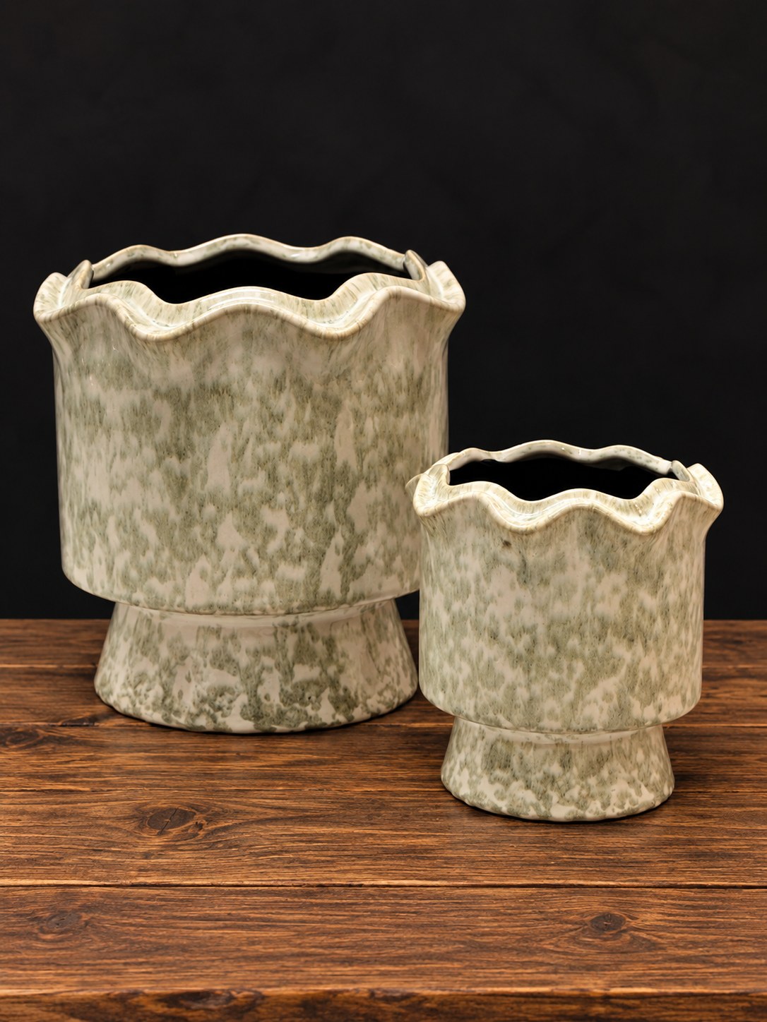 Dos maceteros de cerámica esmaltada verde con borde ondulado, grande y pequeño, sobre mesa de madera